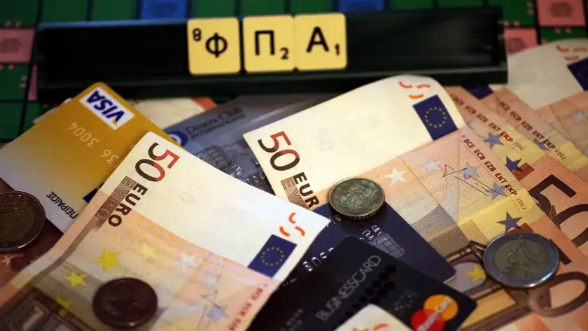 Γράμματα που σχηματίζουν τη λέξη ΦΠΑ πάνω σε χαρτονομίσματα και κάρτες